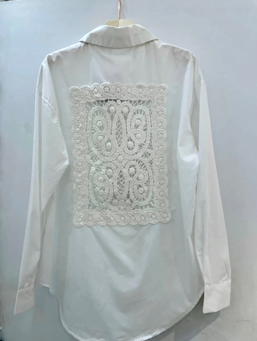 White collared shirt with crochet detail on the back, button up closure with long sleeves.